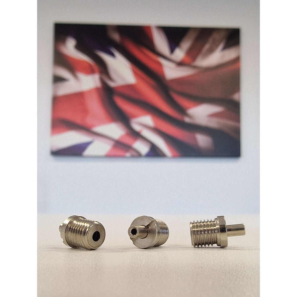 Three Metallic TECNI cable Grippers on a white table with a blurred union jack background 170.012.002