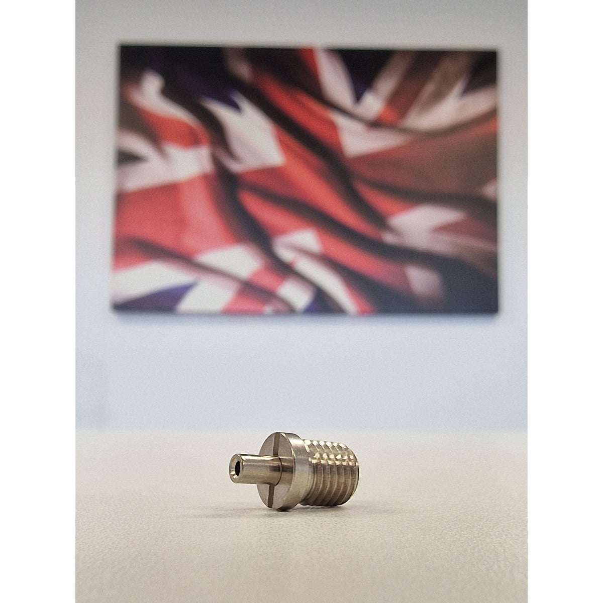 Metallic TECNI cable Gripper on a white table with a blurred union jack background 170.012.002