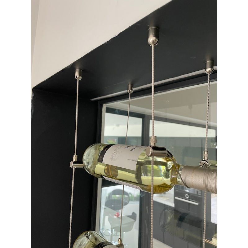 Wine rack installation with a black border in front of a window. Metallic mechanical components and cable used to suspend wine bottles. 170.025.004