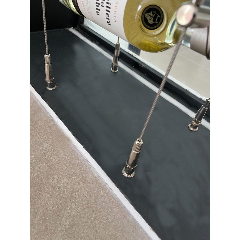 Metallic tension grippers holding wire rope cables on a black floor as part of a wine rack system in a home 170.025.004