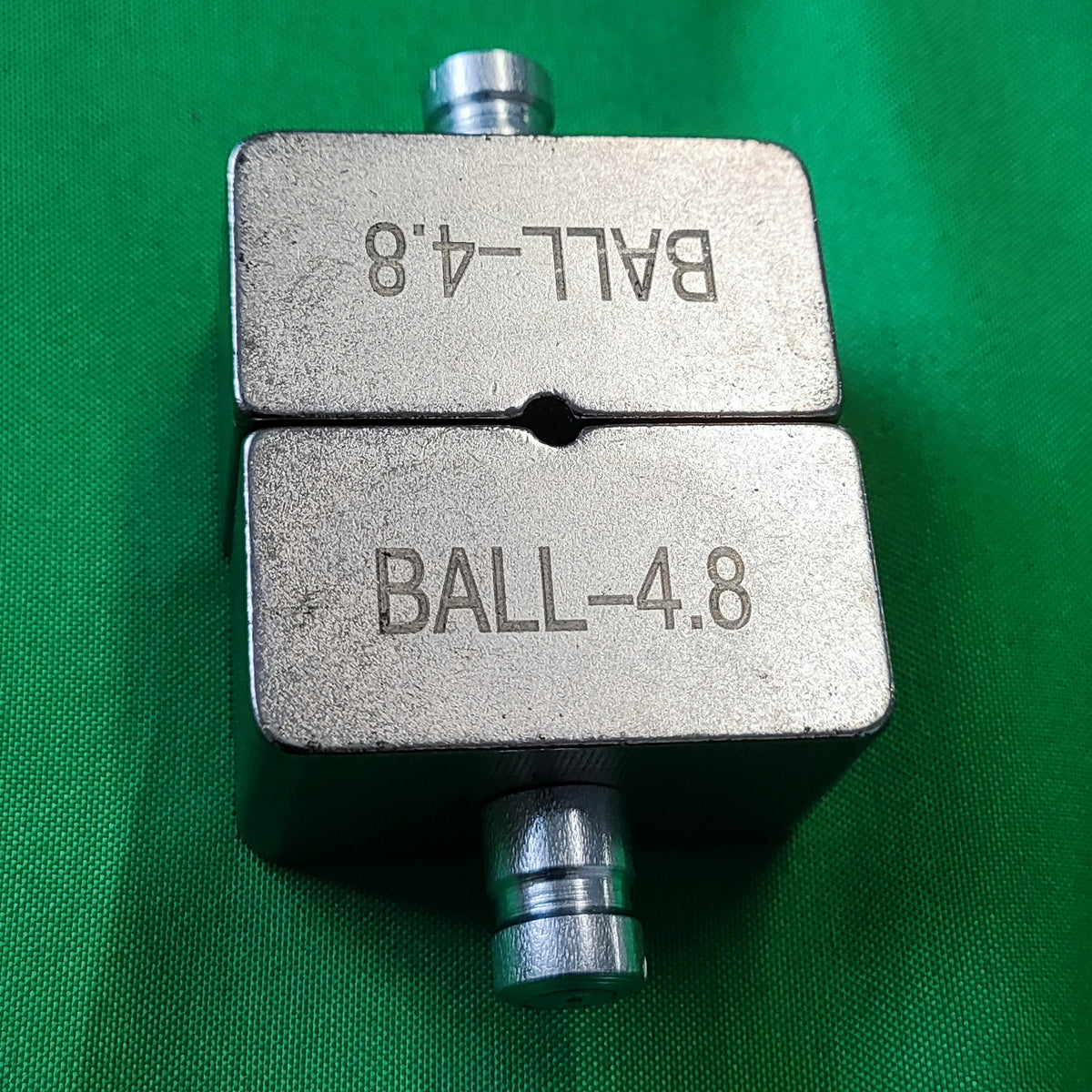 Photo of a ball die set put together showing the gab and top and bottom fitted together. Showing engraving marks on green background. 