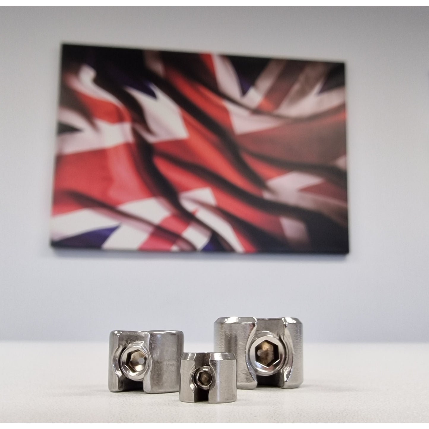 3 Stainless Steel DIY stop fittings on a table with a flag background. TECNI 341.710.