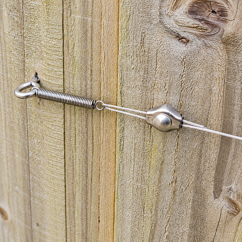 Close up photo of a trellis tension spring on a wooden fence showing the components all assembled together. 