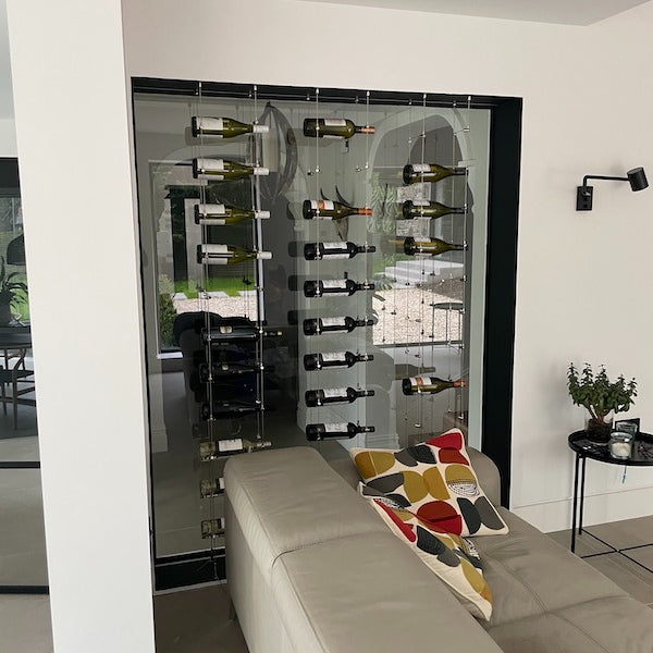 Metallic tension grippers holding wire rope cables on a black floor in a window as part of a wine rack system in a home 170.025.004
