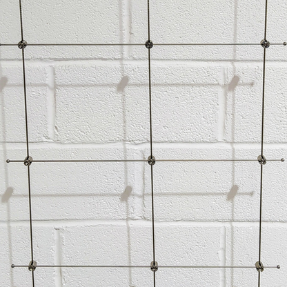 Photo showing a trellis assembly made onto a white wall showing the different components put altogether in a grid. 