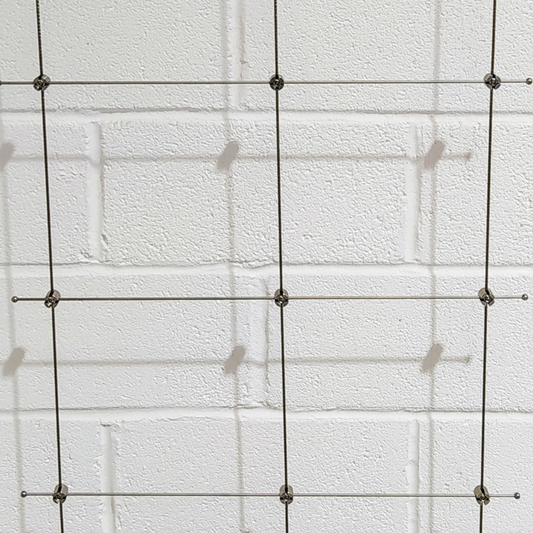 Photo showing a trellis assembly made onto a white wall showing the different components put altogether in a grid. 