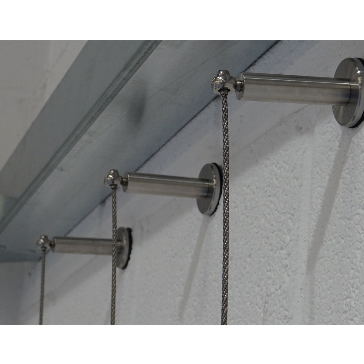 Photo showing three pillar trellis components into a white brick wall with cable assembled from the pillars. 