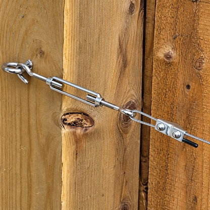 A close up photo of a stainless steel turnbuckle and other components from the trellis kit put altogether on weathered wood. 